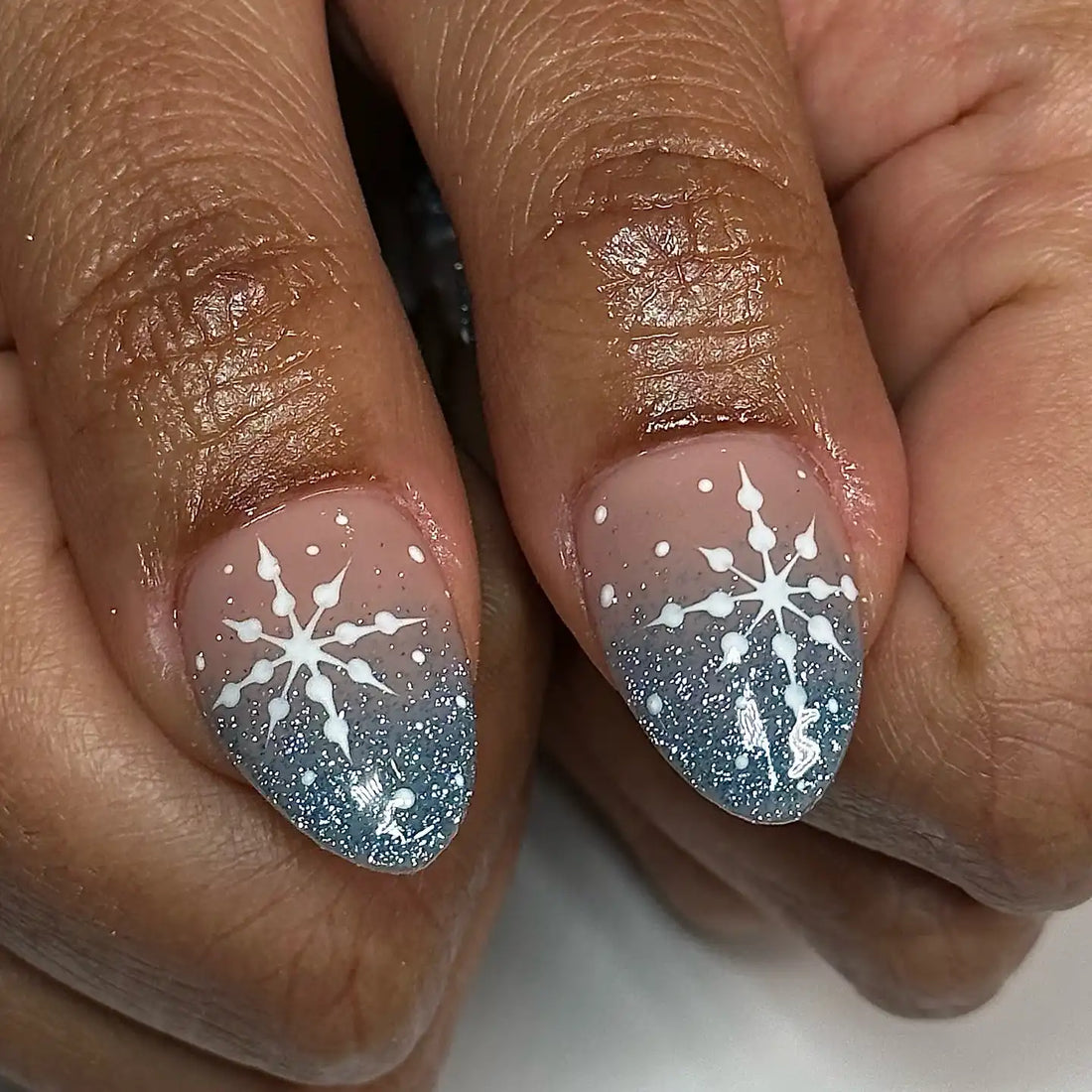 Handmade winter press-on nails with blue glitter ombre and white snowflake designs.